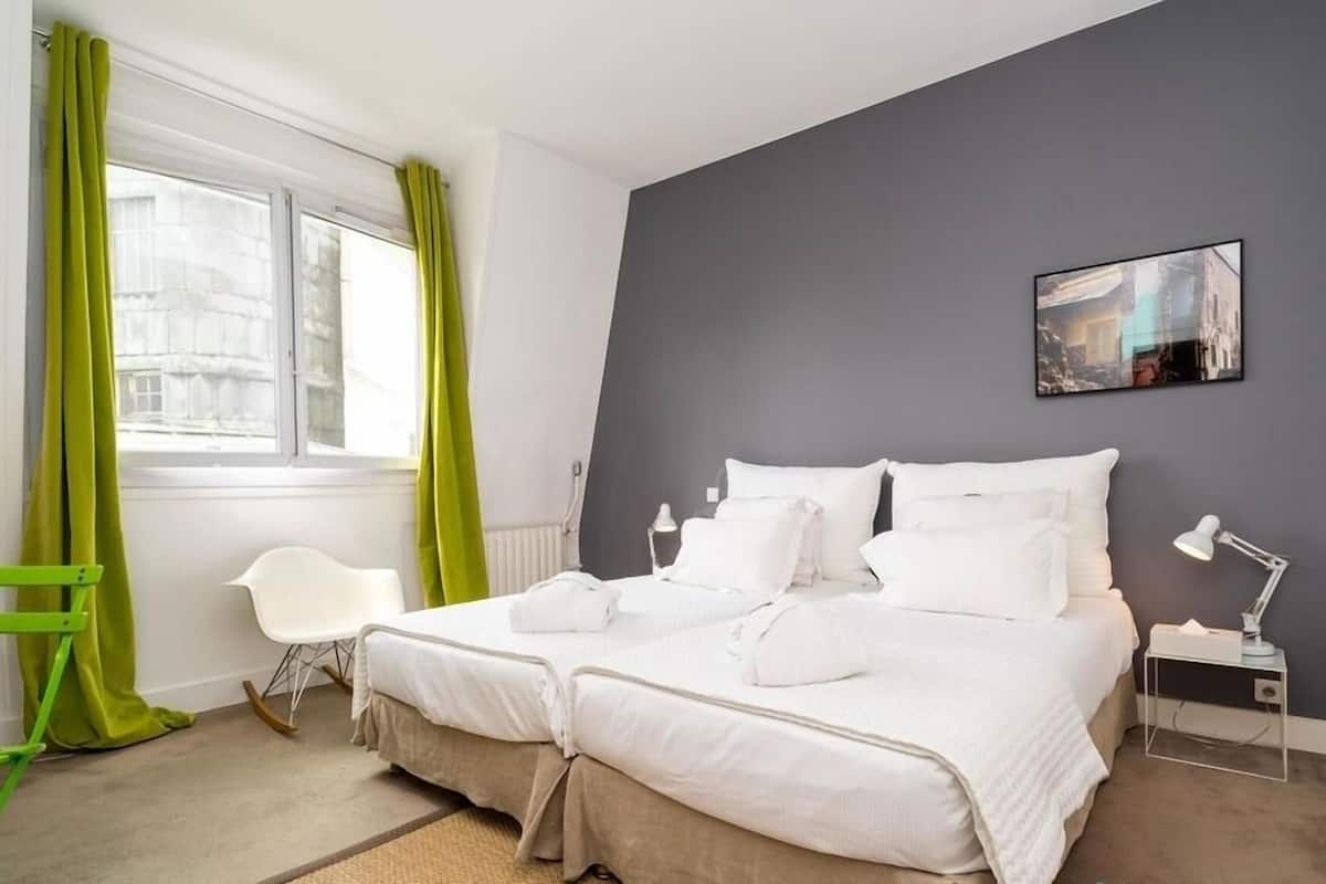 Una habitación de hotel con una cama, una silla, un escritorio, una lámpara y un cuadro en la pared.