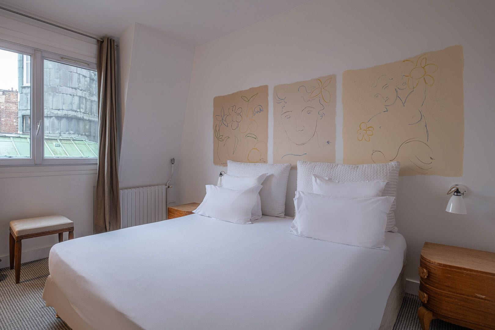 Une chambre d’hôtel avec un grand lit, deux tables de chevet, une fenêtre avec des rideaux et des œuvres d’art murales.