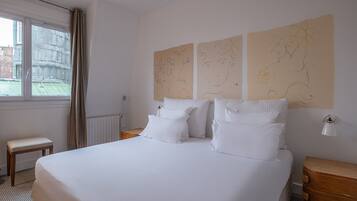 Une chambre d’hôtel avec un grand lit, deux tables de chevet, une fenêtre avec des rideaux et des œuvres d’art murales.