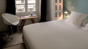 A hotel room with a bed, a chair, a desk with a lamp, and a window with curtains. - Hôtel Arvor Saint Georges (Paris)