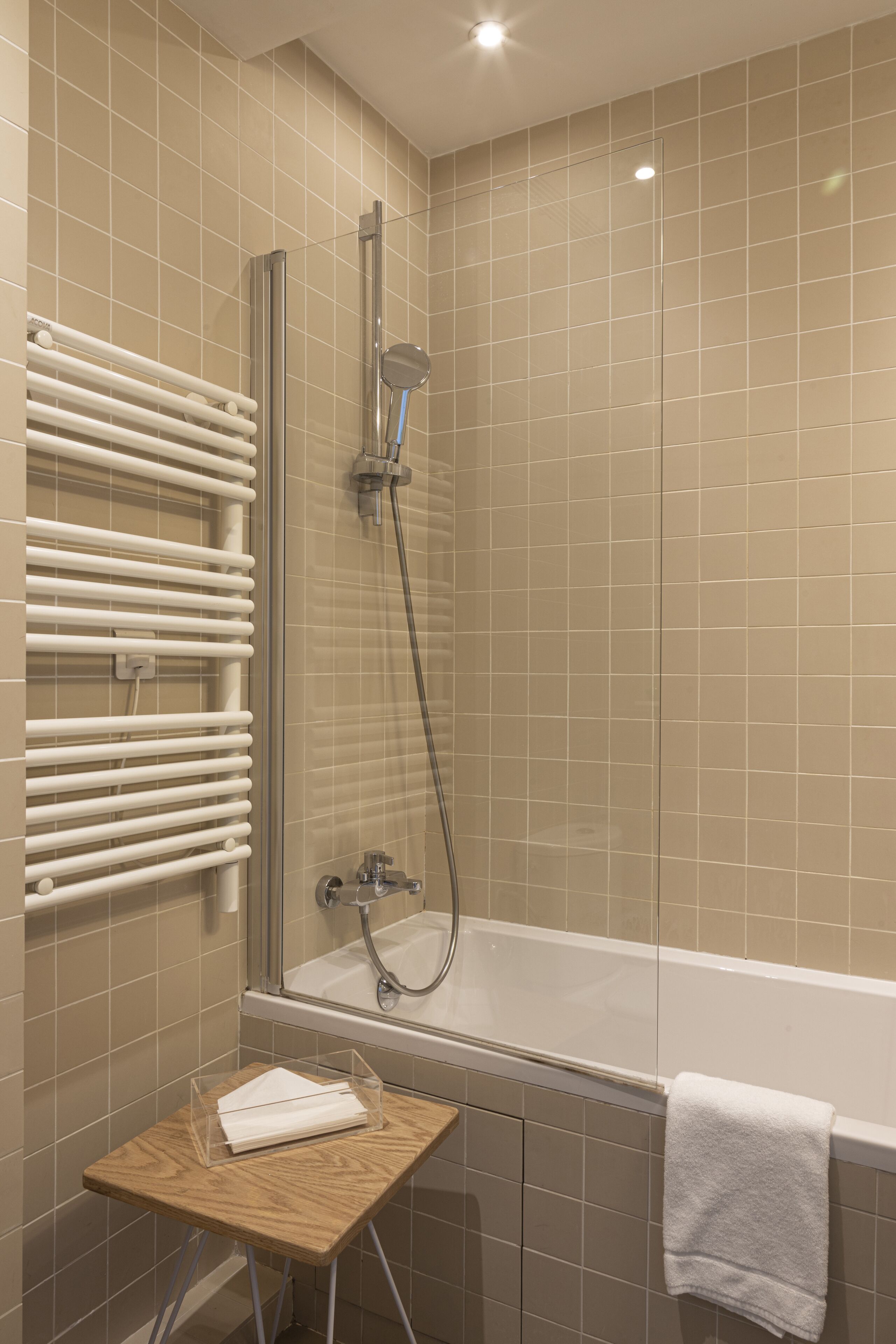 A bathroom with a glass-enclosed shower, a bathtub, and a wooden stool with a towel.