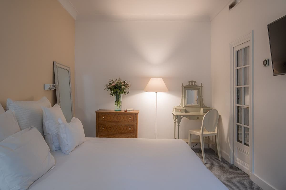 Una habitación de hotel con cama, cómoda, escritorio, silla, lámpara, espejo y televisor.