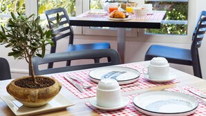 A dining table with chairs, a potted plant, and a breakfast setting with plates, cups, and a fruit bowl. - Hôtel la Rotonde (La Croix-Valmer)