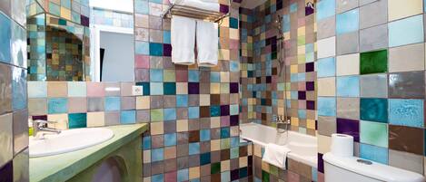 Casa de banho com parede em mosaico de azulejos, pia, banheira e sanita.