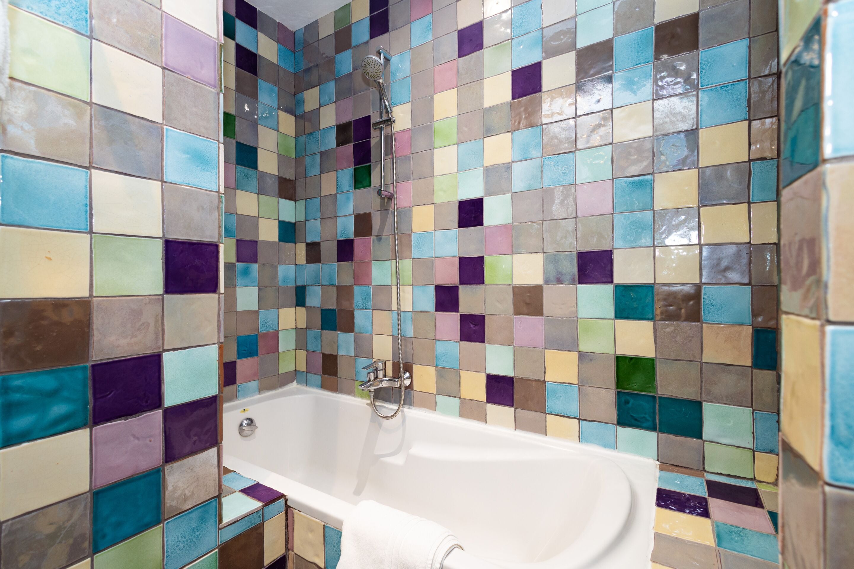 A bathroom with a tiled shower wall and a white bathtub.