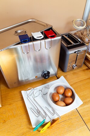 A kitchen with a stainless steel toaster, a bowl of eggs, and kitchen utensils on a wooden table.