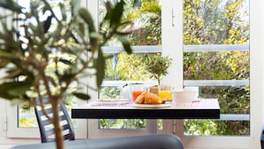 A dining area with a table, chairs, a potted plant, and a view through large windows. - Hôtel la Rotonde (La Croix-Valmer)