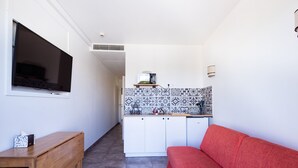 A compact living space with a kitchenette, a flat-screen TV, a red sofa, and a wooden table. - Hôtel la Rotonde (La Croix-Valmer)
