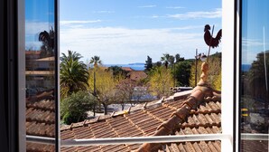 A view through a window of a tiled roof, palm trees, and a distant coastline. - Hôtel la Rotonde (La Croix-Valmer)