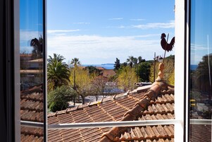 Vista a través de una ventana que muestra un tejado de baldosas, palmeras y una costa distante.