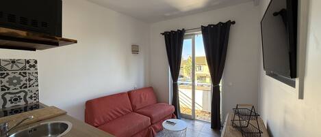 Una cocina compacta con lavamanos, un sofá rojo, una pequeña mesa redonda y un televisor montado en la pared.