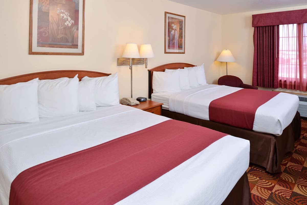 Two double beds with white and red linens, bedside lamps, a telephone, and framed artwork on the walls.