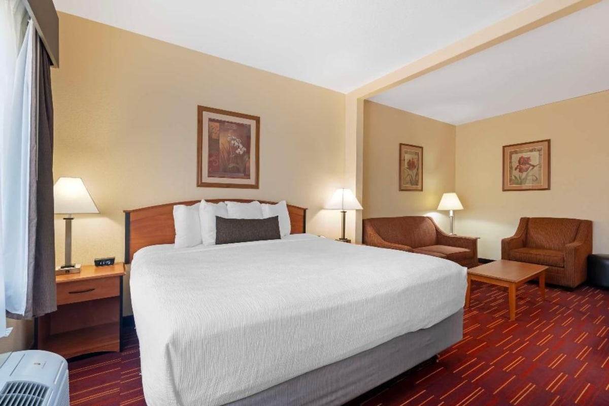 A hotel room with a large bed, two armchairs, a small table, and a desk with a lamp.