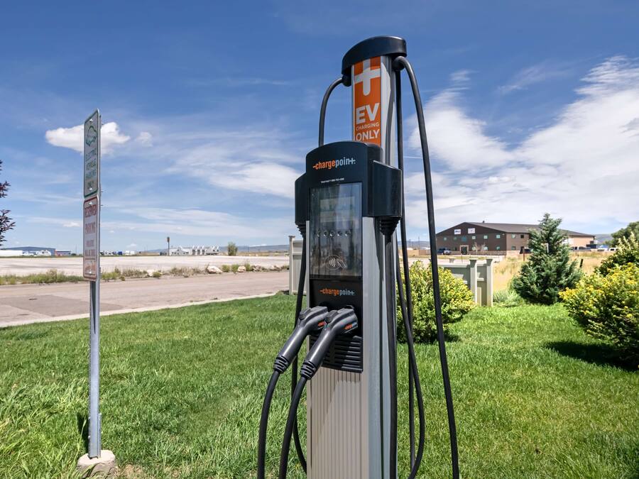 Eine EV-Ladestation mit deutlicher Beschriftung, die ausschließlich für Elektrofahrzeuge zugänglich ist, befindet sich in einer Grünfläche mit einem Gebäude im Hintergrund.