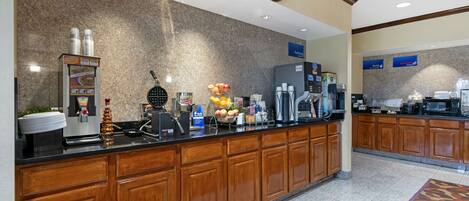 A hotel reception area with a coffee machine, fruit display, and a clock on the wall.