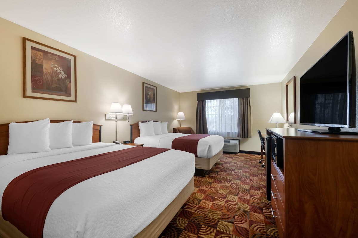Quarto de hotel com duas camas, televisão, mesa de trabalho e janela com cortinas.