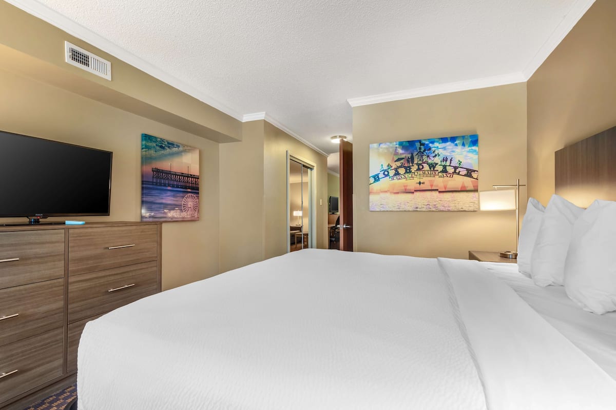 A hotel room with a large bed, a flat-screen TV, wooden cabinets, and artwork on the walls.