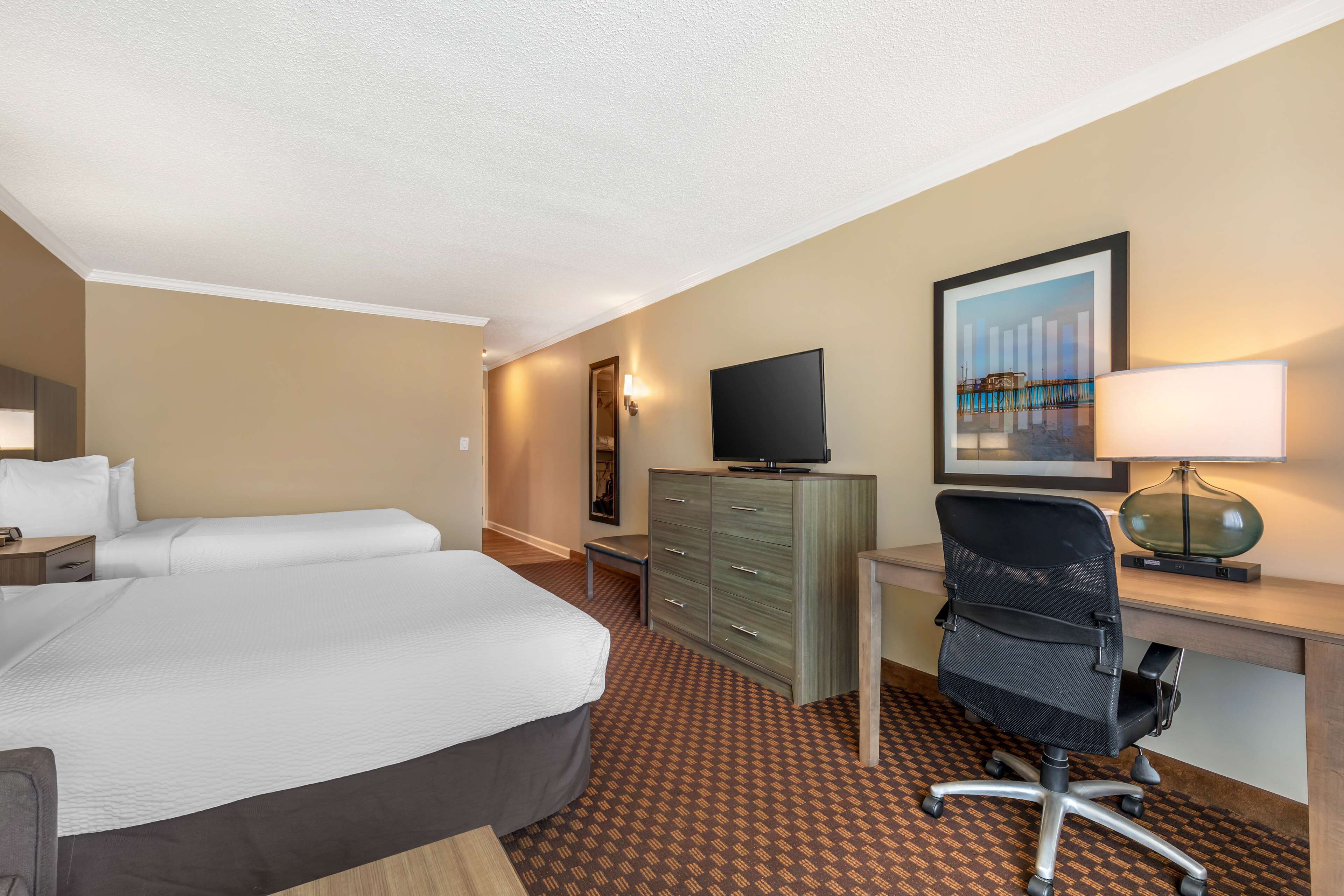 Une chambre d’hôtel équipée d’un lit, d’un bureau, d’une chaise, d’une télévision et d’œuvres d’art accrochées au mur.