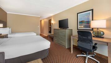 A hotel room with a bed, desk, chair, television, and artwork on the wall.