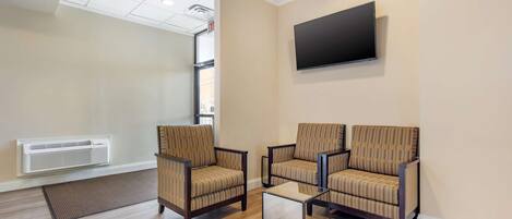 A room with two armchairs, a coffee table, a mounted TV, and a wall-mounted air conditioner.