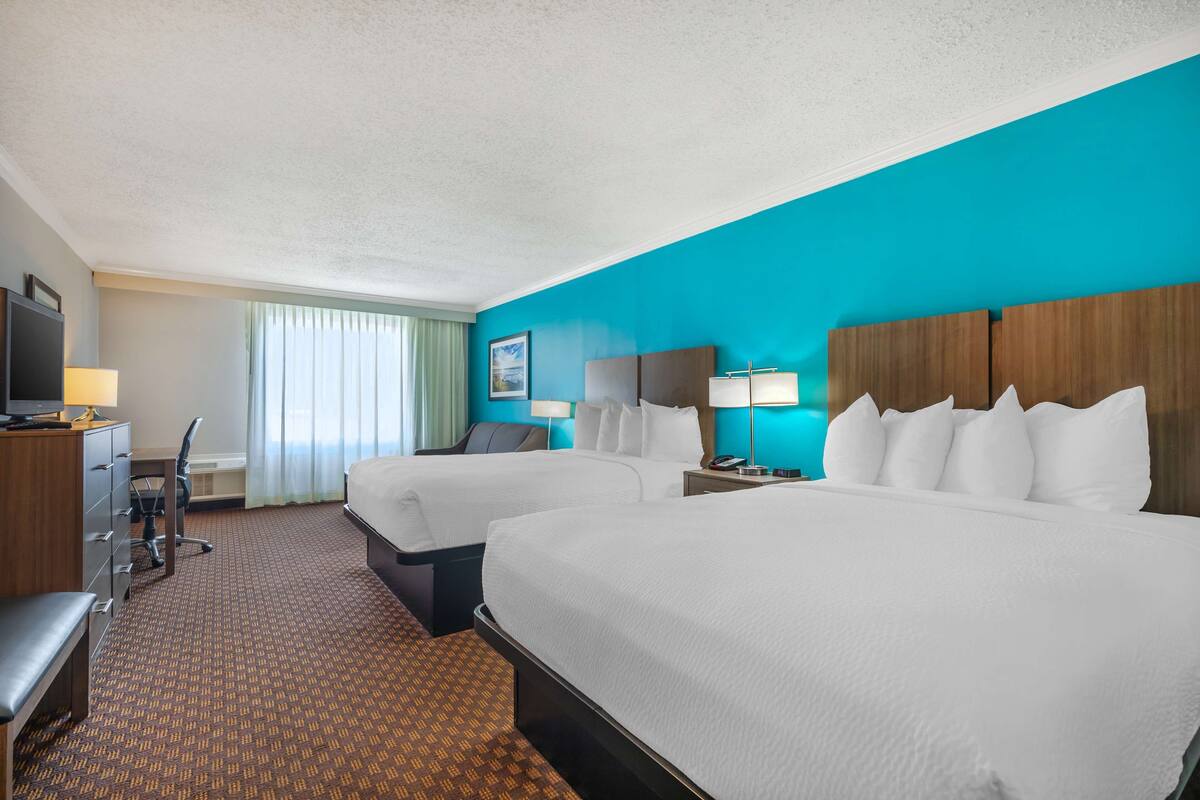 A hotel room with two beds, a desk, a chair, and a television.