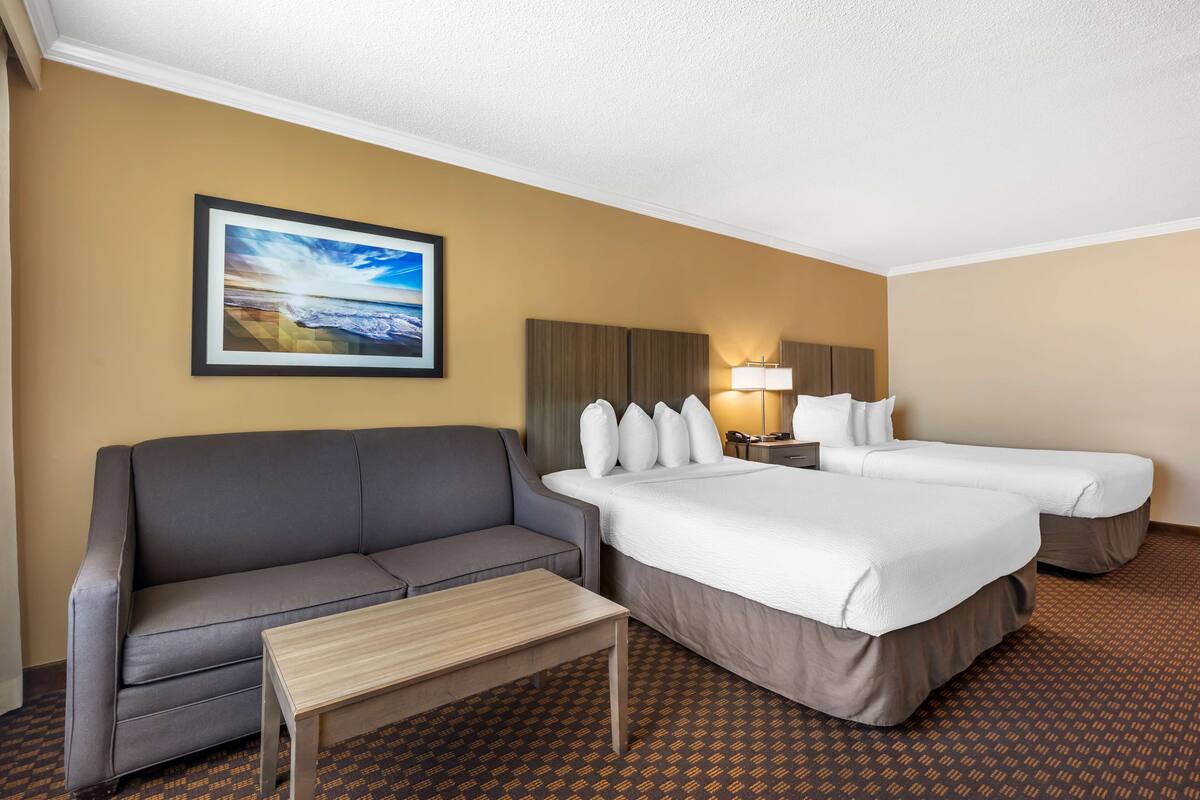 A hotel room with a sofa, two beds, a small table, a nightstand, and a framed picture on the wall.