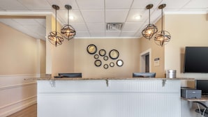 A reception area with a white reception desk, two black chairs, a flat-screen TV, and a wall-mounted clock. - Best Western Ocean City Hotel & Suites (Ocean City)