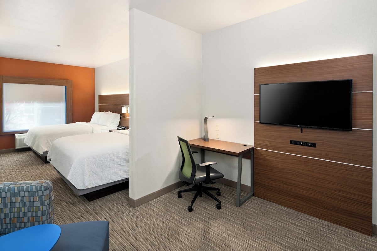 A hotel room with two beds, a desk, a chair, a flat-screen TV, and a large window.