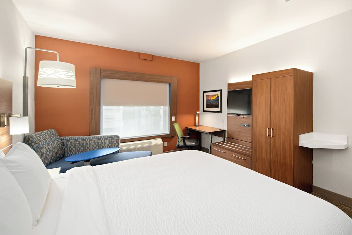 A hotel room with a large bed, a desk, a chair, a TV, and a wardrobe.