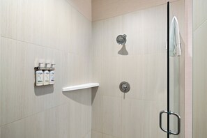 A shower area with a glass door, a towel hanging on the door, and toiletries on a shelf. - Holiday Inn Express & Suites Interstate 90 by IHG (Coeur d'Alene)