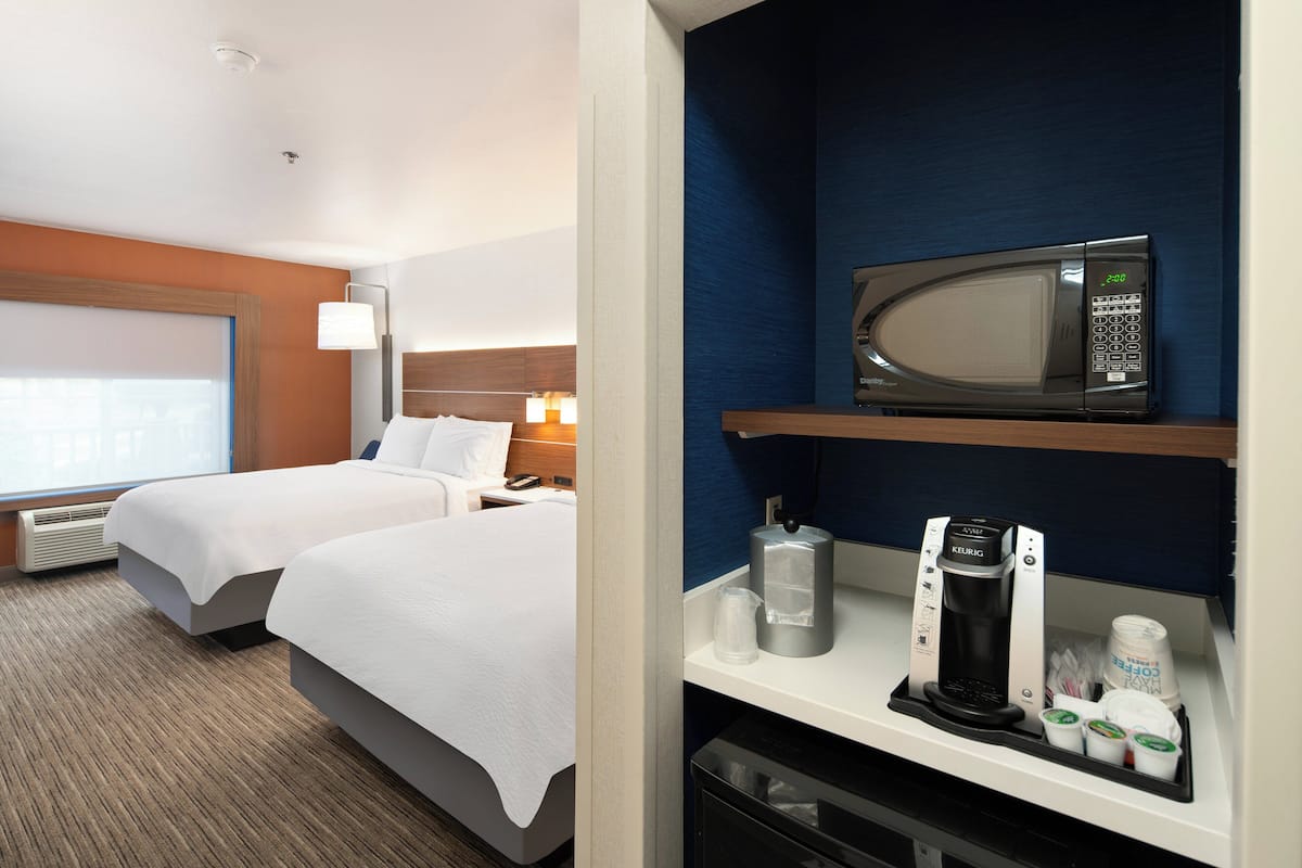 A hotel room with two beds, a minibar, a microwave, and a coffee maker.