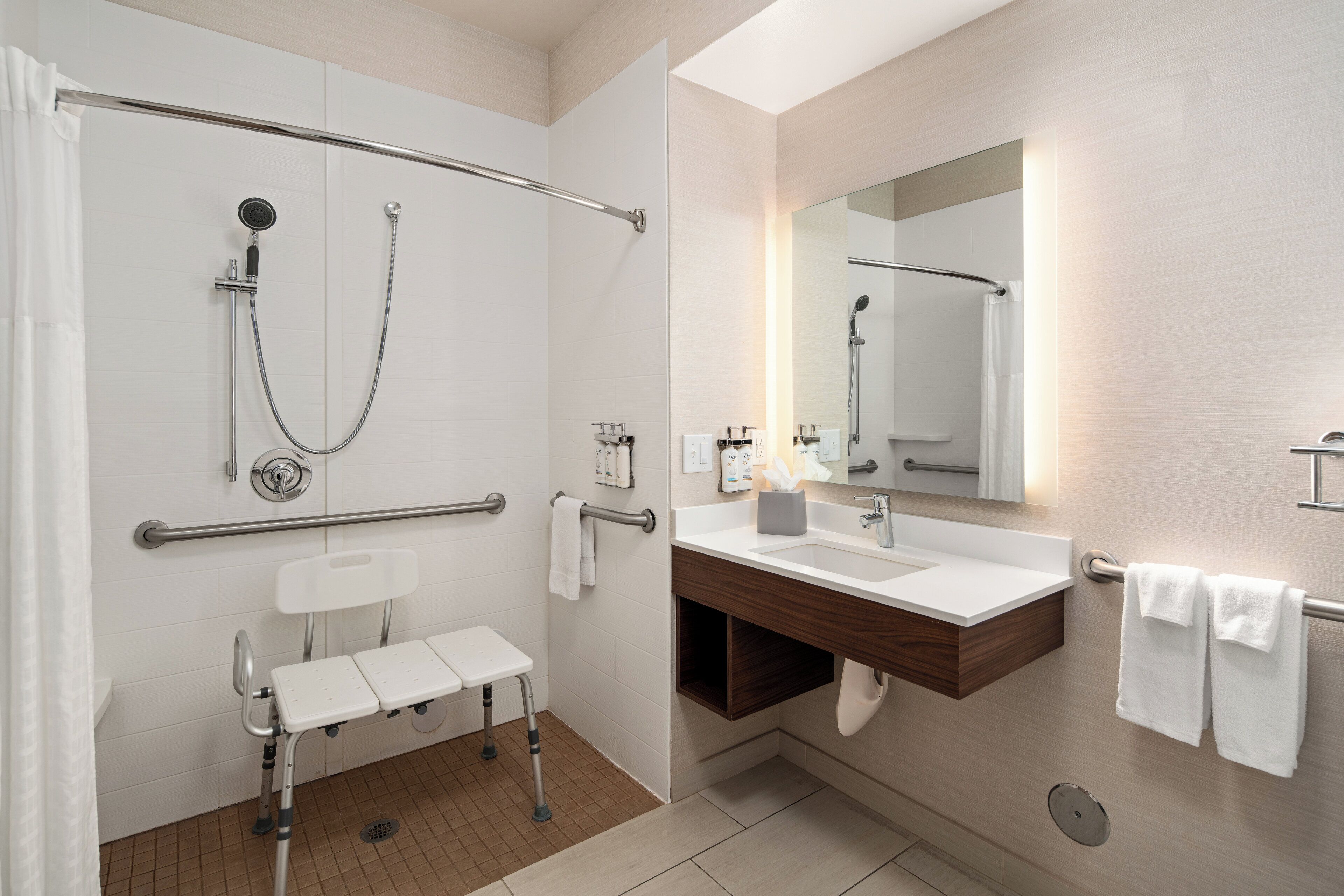 A modern bathroom with a shower, a vanity with a mirror, and a wheelchair-accessible bench.