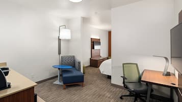 Habitación de hotel con escritorio, una silla azul, una silla verde, cama y televisor.
