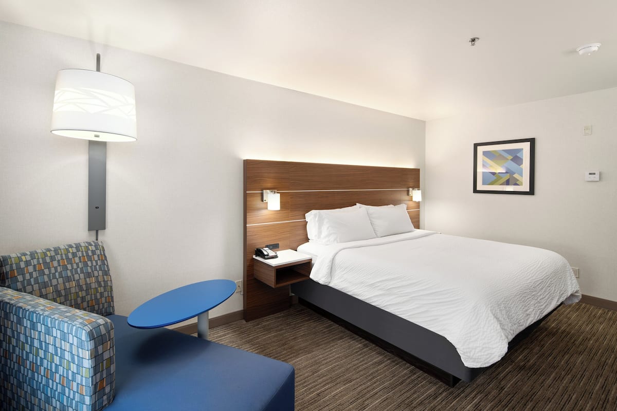 A hotel room with a bed, a nightstand, a desk, a chair, and a wall-mounted lamp.