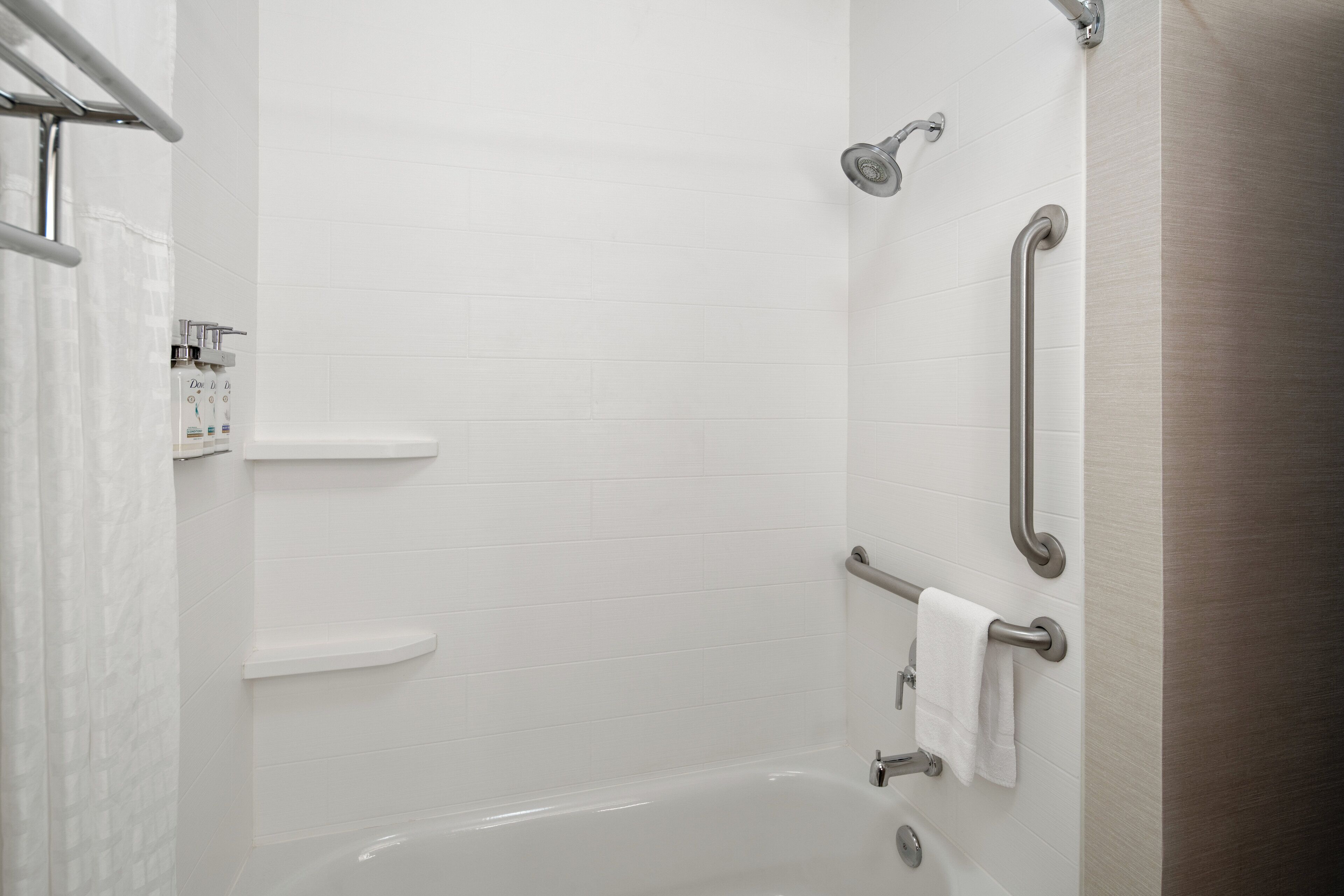 A modern bathroom with white tiles, a bathtub, and grab bars for accessibility.