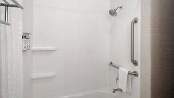 A modern bathroom with white tiles, a bathtub, and grab bars for accessibility.