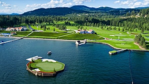 An aerial view of a golf course with a water body, surrounded by forested hills and residential areas. - Holiday Inn Express & Suites Interstate 90 by IHG (Coeur d'Alene)
