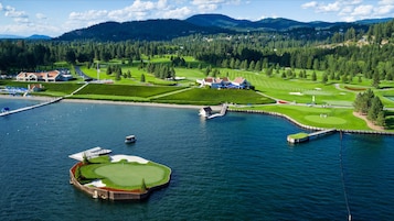An aerial view of a golf course with a water body, surrounded by forested hills and residential areas.