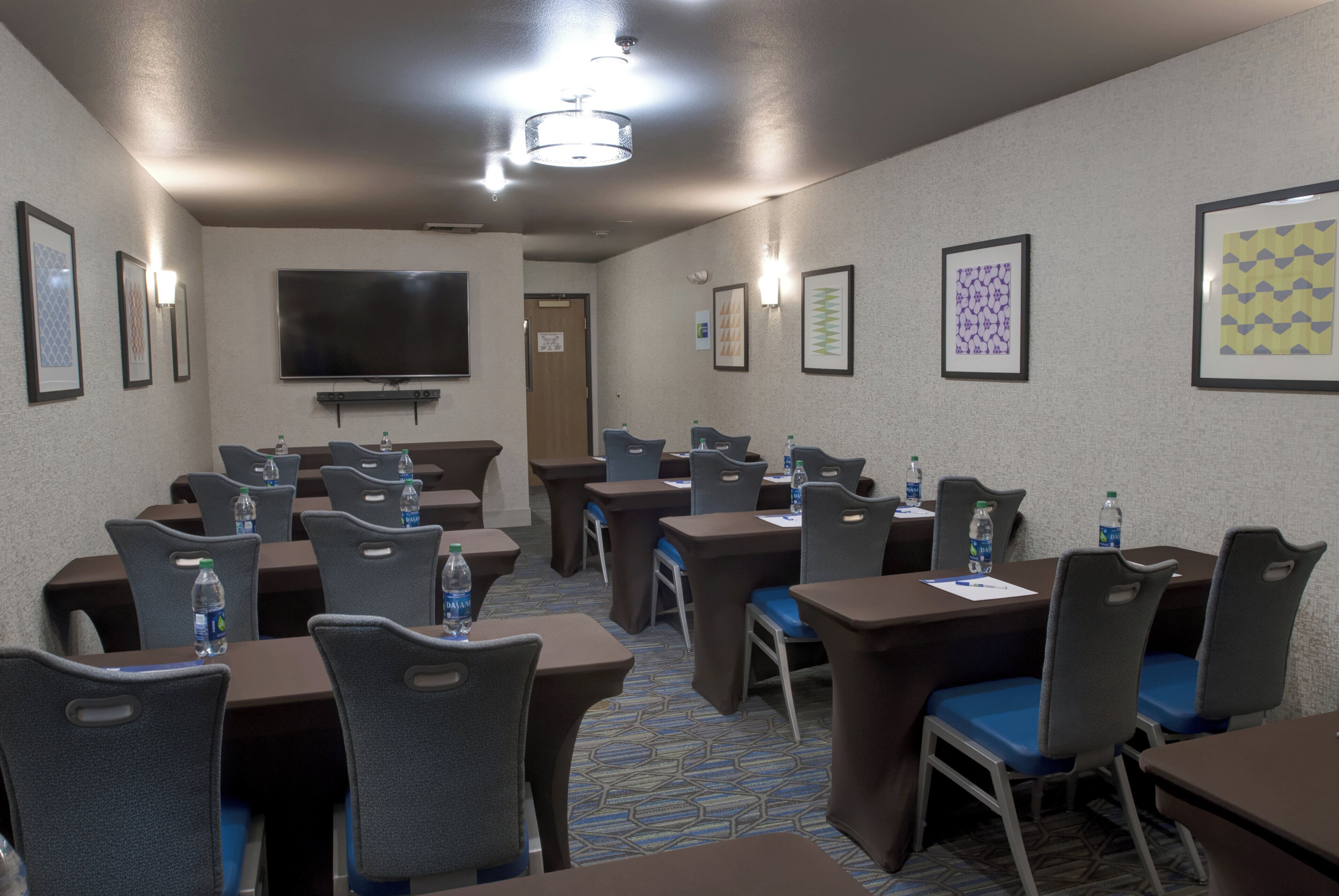 A conference room with tables, chairs, a flat-screen TV, and framed artwork on the walls.