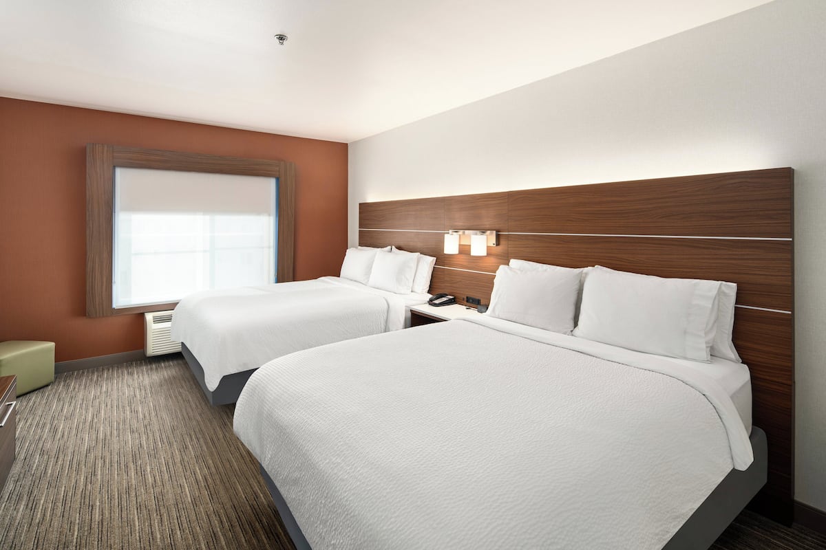 A hotel room with two beds, a large window, and a wall-mounted light fixture.