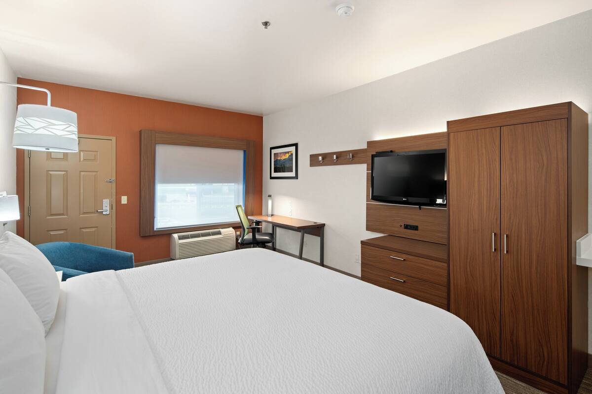 A hotel room with a large bed, a desk, a television, and a wardrobe.