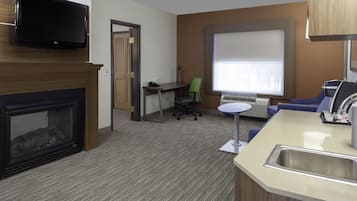 Habitación de hotel moderna con chimenea, televisor de pantalla plana, escritorio con silla, una mesita redonda y lavamanos.