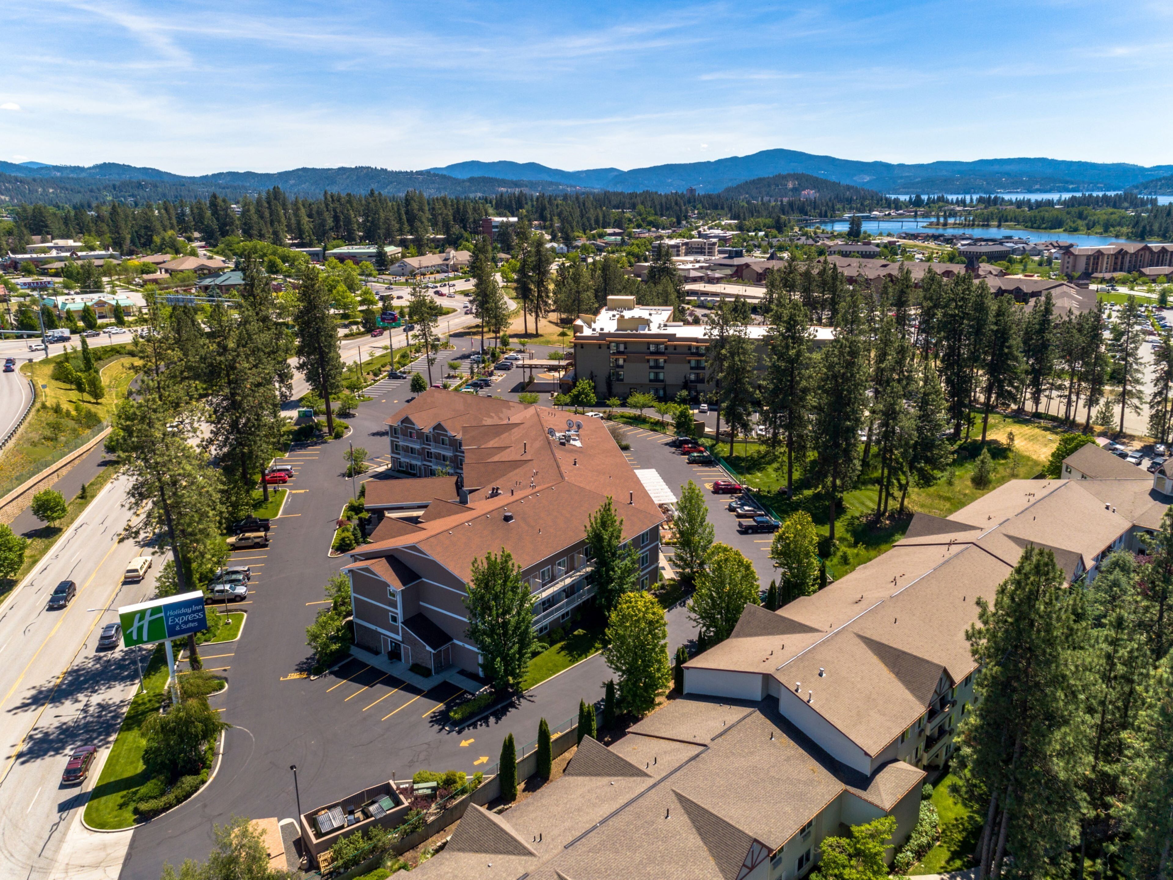 A Holiday Inn Express & Suites with a parking lot, surrounded by trees and a mountainous backdrop.