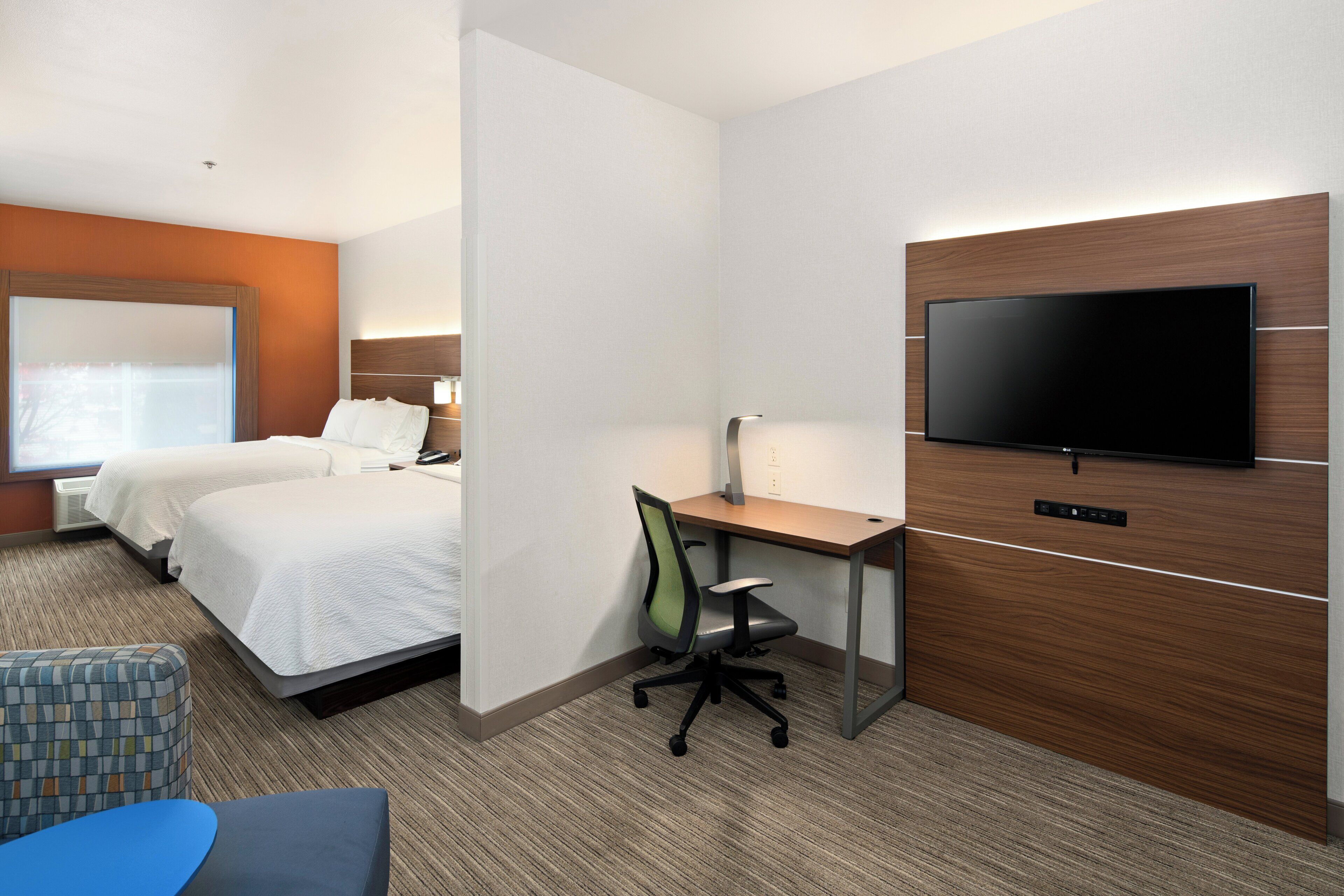 A hotel room with two beds, a desk, a chair, a flat-screen TV, and a large window.