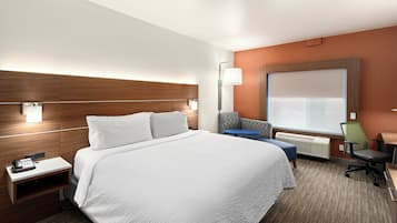 A hotel room with a large bed, a desk with a chair, a small table, and a window with blinds.