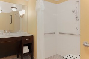 Ein Badezimmer mit einem weißen Waschbecken, Spiegel und Dusche. Handtuchhalter und ein Duschkopf sind vorhanden.