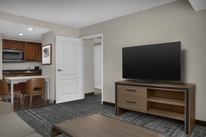 Ett hotellrum med ett litet kök, en platt-TV, en sittgrupp med ett soffbord och ett golv med heltäckningsmatta.