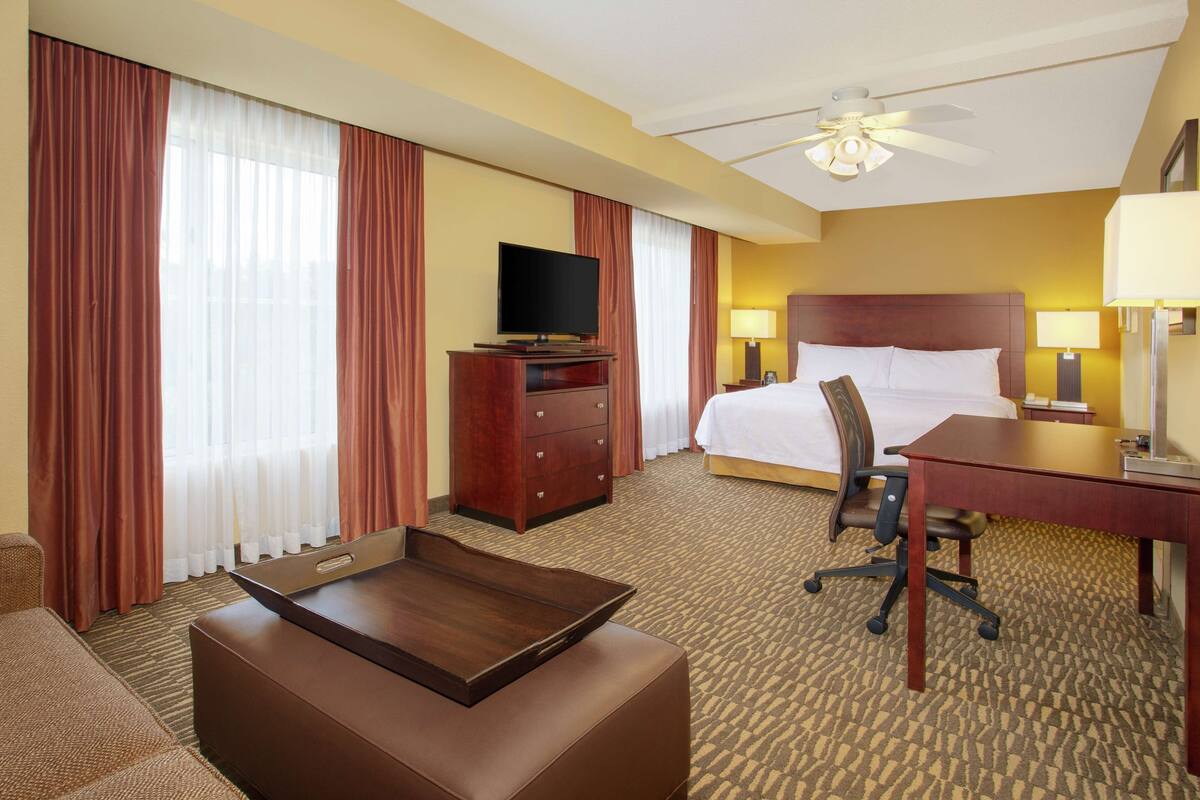 Une chambre d’hôtel équipée d’un lit, d’un bureau, d’une chaise, d’une télévision et d’un ventilateur de plafond.