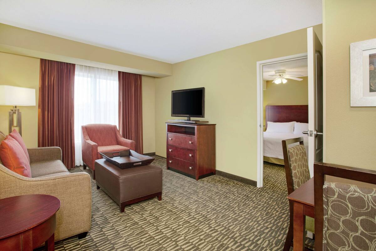 Une chambre d’hôtel comprenant un canapé, un fauteuil, un pouf, une télévision, une commode et un lit.