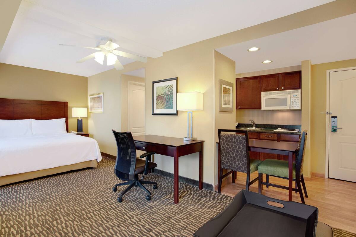 Une chambre d’hôtel équipée d’un lit, d’un bureau, d’une chaise de bureau, d’une kitchenette et d’un ventilateur de plafond.